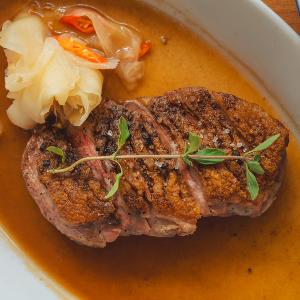 Sliced duck breast with crispy skin, herbs, and pickled ginger in a savory sauce.