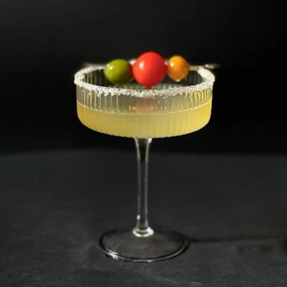 A Teakwood Thai Chophouse cocktail in a ribbed glass, garnished with colorful berries and a salted rim.