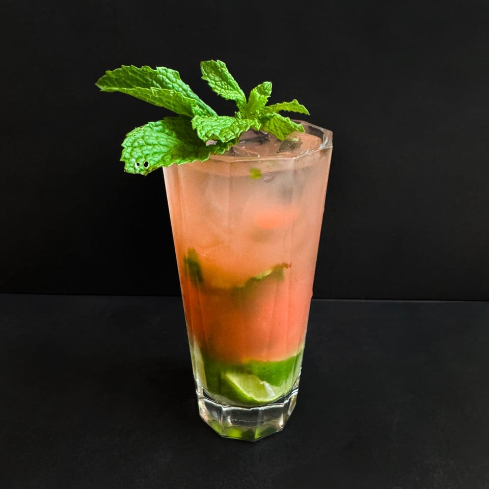 A vibrant pink and green cocktail with mint and lime slices in a tall glass.
