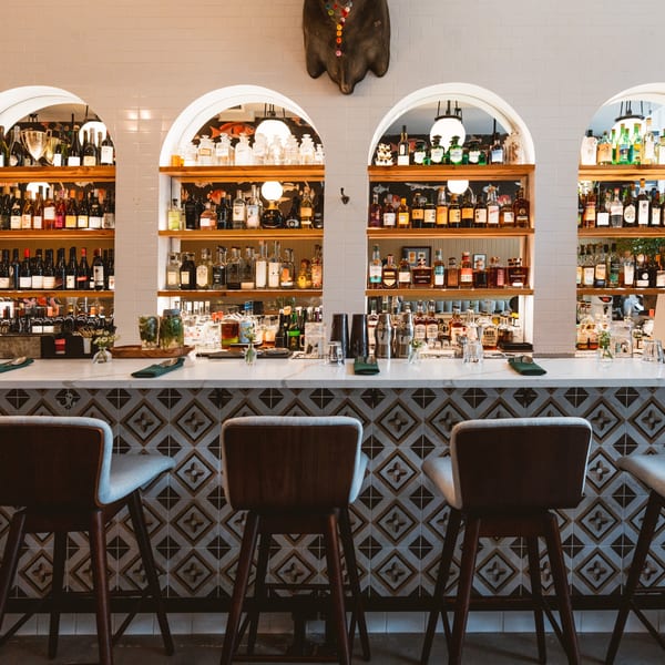 Teakwood Thai Chophouse bar with arched shelves displaying bottles, a marble counter, and patterned tile.