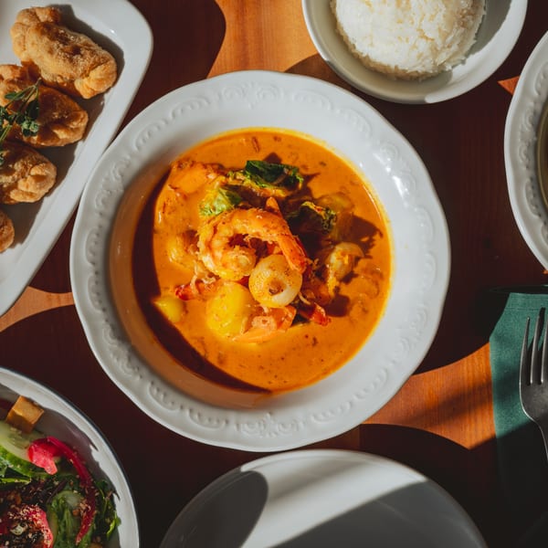 Teakwood Thai Chophouse's red curry with shrimp, rice, fried appetizers, and salad on a wooden table.