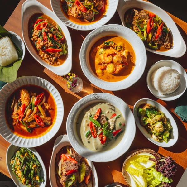 A vibrant spread of various Thai dishes, including curries, stir-fries, rice, and vegetables, on a wooden table.