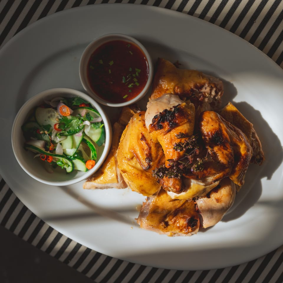 Grilled Thai chicken with two dipping sauces, one with cucumber salad, on a white plate.