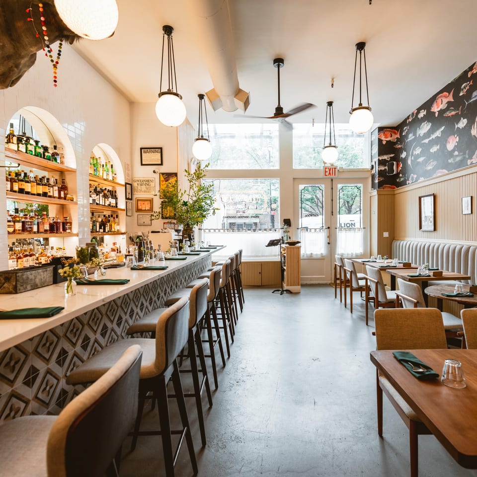 Interior of Teakwood Thai Chophouse, featuring a long bar with stools and dining tables with chairs.