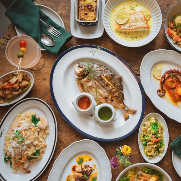 Overhead view of a wooden table laden with various Thai dishes, including whole fish, fried rice, and octopus.