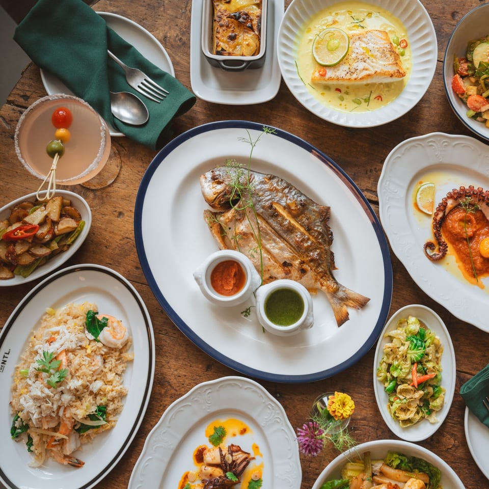 Overhead view of a wooden table laden with various Thai dishes, including whole fish, fried rice, and octopus.