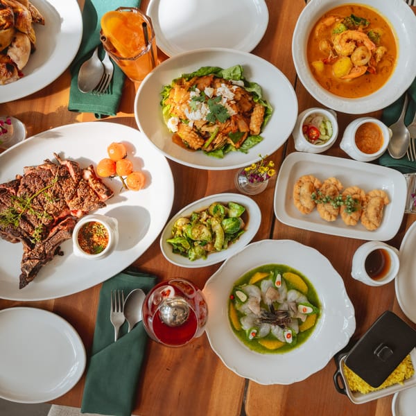 An overhead view of a wooden table laden with various Thai dishes, including steak, curry, and seafood.