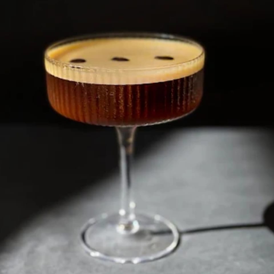 Espresso martini in a coupe glass, topped with foam and three coffee beans.