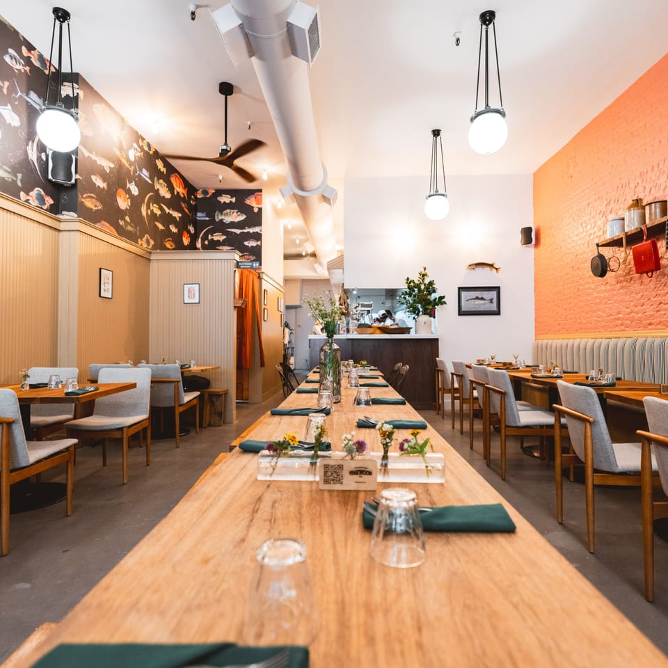 Long wooden tables with green napkins and small floral arrangements in the Teakwood Thai Chophouse dining room.